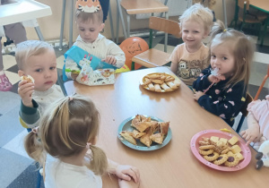 Słodki poczęstunek od jubilata, spożywany przez dzieci przy stolikach.