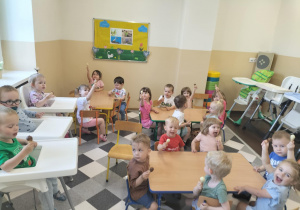 Dzieci jedzą lody przy stolikach.