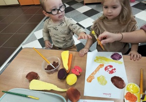 Dzieci przy stolikach robią pracę plastyczną.