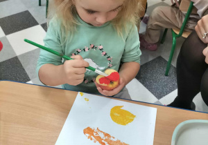 Dzieci przy stolikach robią pracę plastyczną.