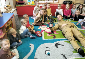 Strażak na leżąco pokazuje dzieciom noktowizier.