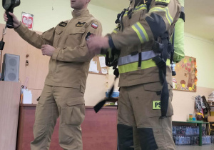 Dwóch strażaków, jeden w mundurze oficjalnym, drugi w nomeksie z butla i maską.