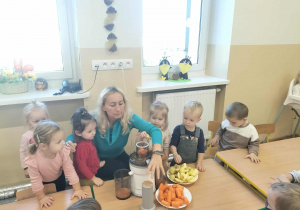 Dzieci przy stoliku z owocami i sokowirówką.