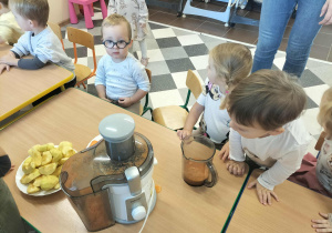 Dzieci przy stoliku z owocami i sokowirówką.
