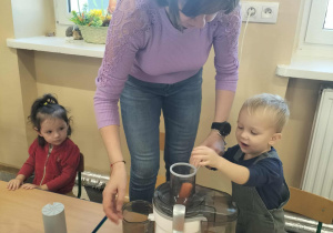 Dzieci przy stoliku z owocami i sokowirówką.