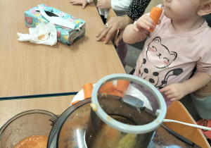 Dzieci przy stoliku z owocami i sokowirówką.