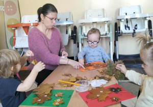 Dzieci przy stoliku lepią liście do kartek i przyczepiają oczka.