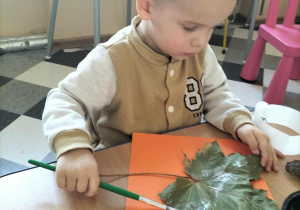 Dzieci przy stoliku lepią liście do kartek i przyczepiają oczka.