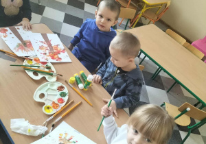 Dzieci malują drzewa przy użyciu własnych rączek.