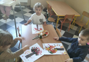 Dzieci malują drzewa przy użyciu własnych rączek.