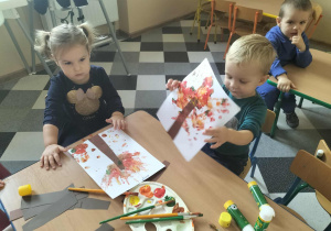 Dzieci malują drzewa przy użyciu własnych rączek.