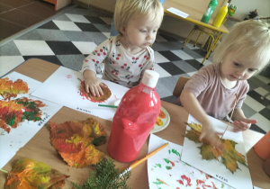 Dzieci przy stolikach malują liście.