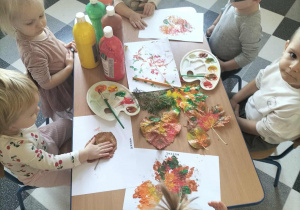 Dzieci przy stolikach malują liście.