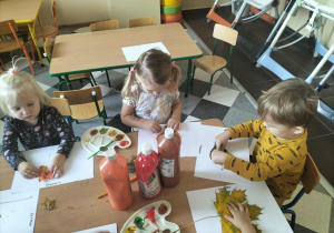 Dzieci przy stolikach malują liście.