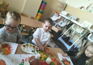 Dzieci przy stolikach malują liście.