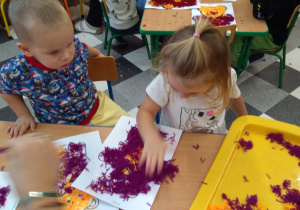 Dzieci przy stolikach robią misia z wełenki.