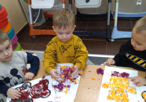 Dzieci przy stolikach robią misia z wełenki.