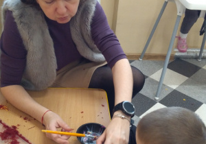 Dzieci przy stolikach robią misia z wełenki.