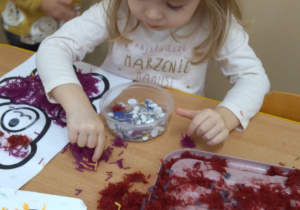 Dzieci przy stolikach robią misia z wełenki.