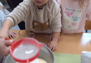 Dzieci z ciocią łączą składniki na pierniki.