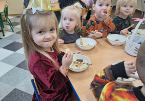 Dzieci biesiadują przy stolikach z poczęstunkiem urodzinowym.