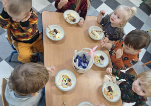 Dzieci biesiadują przy stolikach z poczęstunkiem urodzinowym.