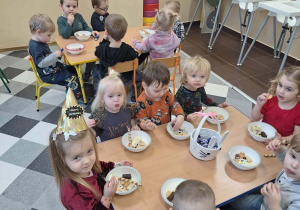 Dzieci biesiadują przy stolikach z poczęstunkiem urodzinowym.