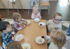 Dzieci siedzą przy stolikach i jedzą posiłek urodzinowy.