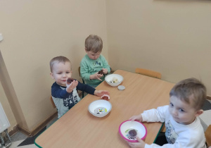 Dzieci siedzą przy stolikach i jedzą posiłek urodzinowy.