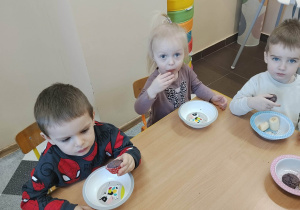 Dzieci siedzą przy stolikach i jedzą posiłek urodzinowy.